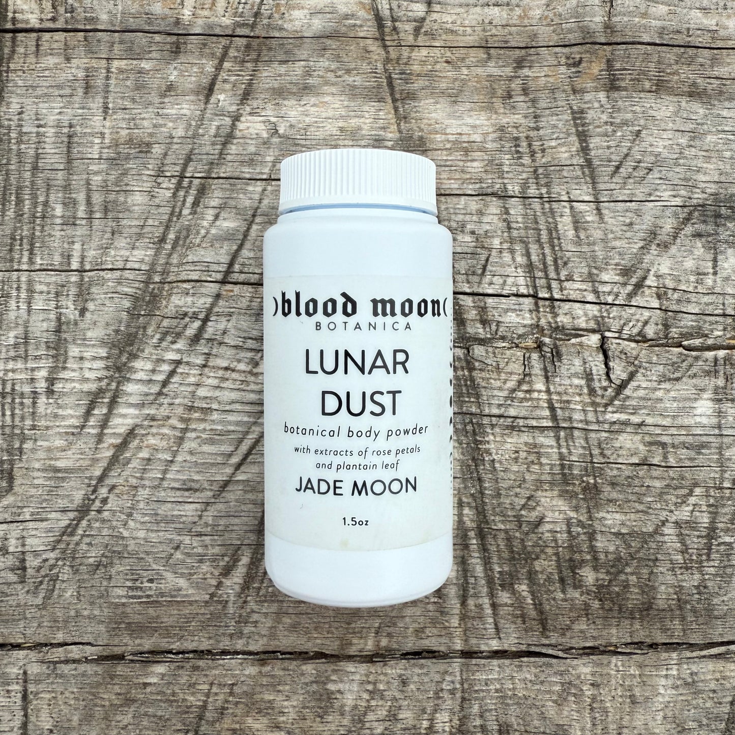 Bottle of 'Lunar Dust' botanical body powder by Blood Moon Botanica on a wooden surface